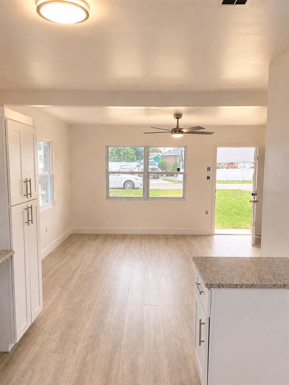 A kitchen and living area with light wood-look flooring, white cabinets, and a ceiling fan — 736 HULL STREET, LAKELAND, FL
