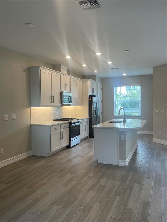 A modern kitchen features white cabinetry, stainless steel appliances, a center island, and wood-look flooring — 4596 ALMADA LANE, WESLEY CHAPEL, FL