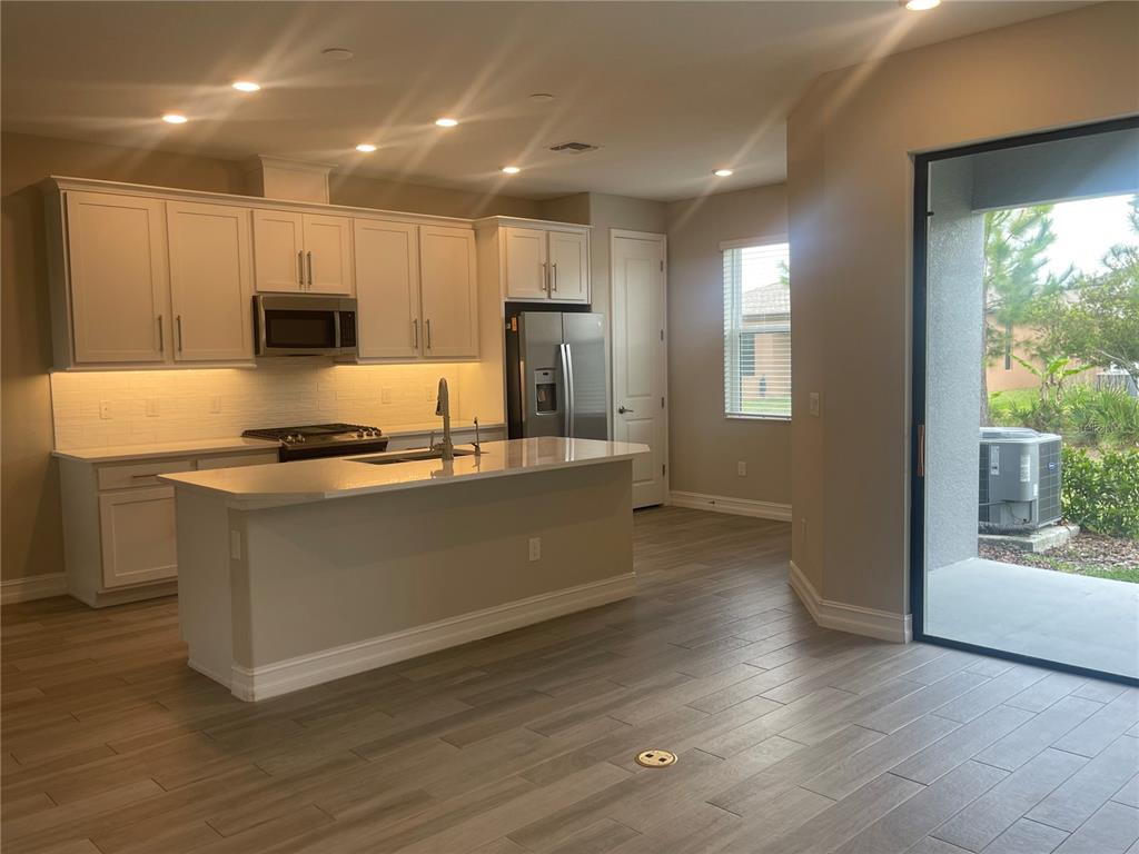 A modern kitchen features white cabinets, stainless steel appliances, a center island, and wood-look flooring — 4596 ALMADA LANE, WESLEY CHAPEL, FL