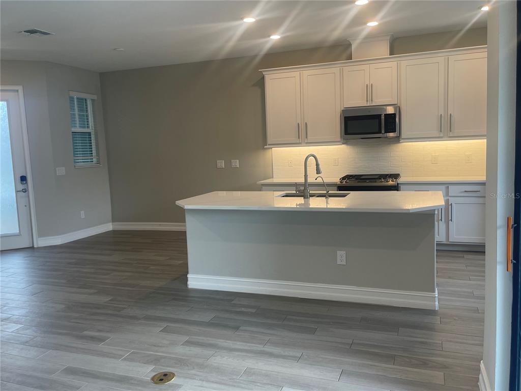 A kitchen features white cabinets, a central island with a sink, and light wood-look flooring — 4596 ALMADA LANE, WESLEY CHAPEL, FL