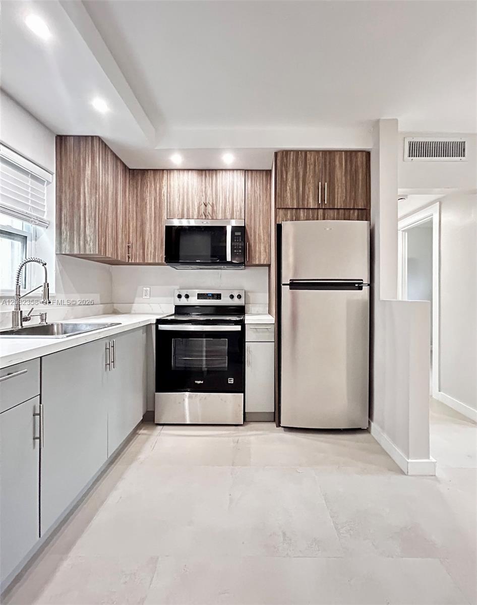 A kitchen features light gray lower cabinets, wood-grain upper cabinets, and stainless steel appliances — 1301 N 12th Ct # 10A, Hollywood FL 33019, HOLLYWOOD, FL