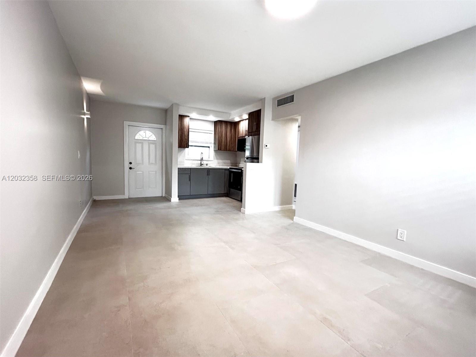 An open-concept living area features light-colored tile flooring, gray walls, and a small kitchen — 1301 N 12th Ct # 10A, Hollywood FL 33019, HOLLYWOOD, FL