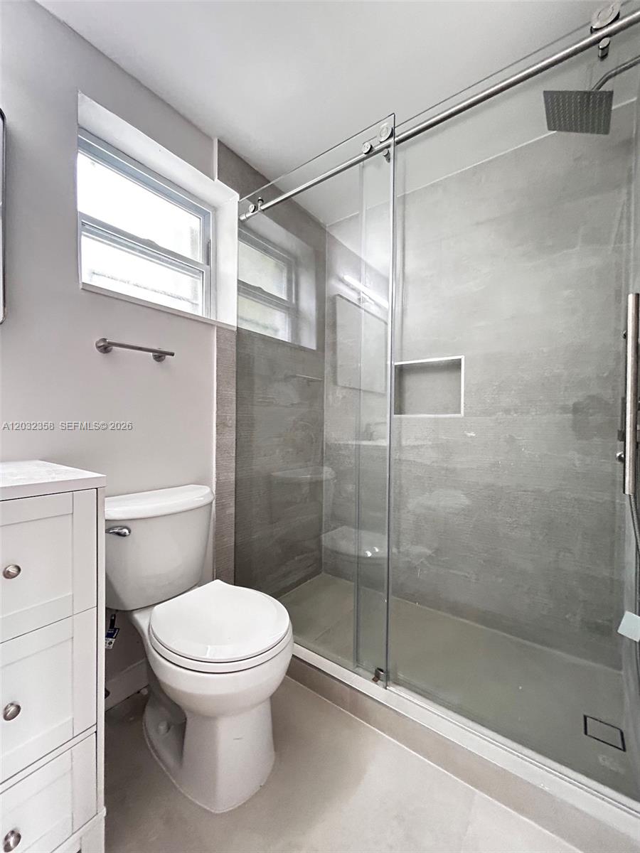 A bathroom features a white toilet, a glass-enclosed shower with gray tile, and a vanity — 1301 N 12th Ct # 10A, Hollywood FL 33019, HOLLYWOOD, FL