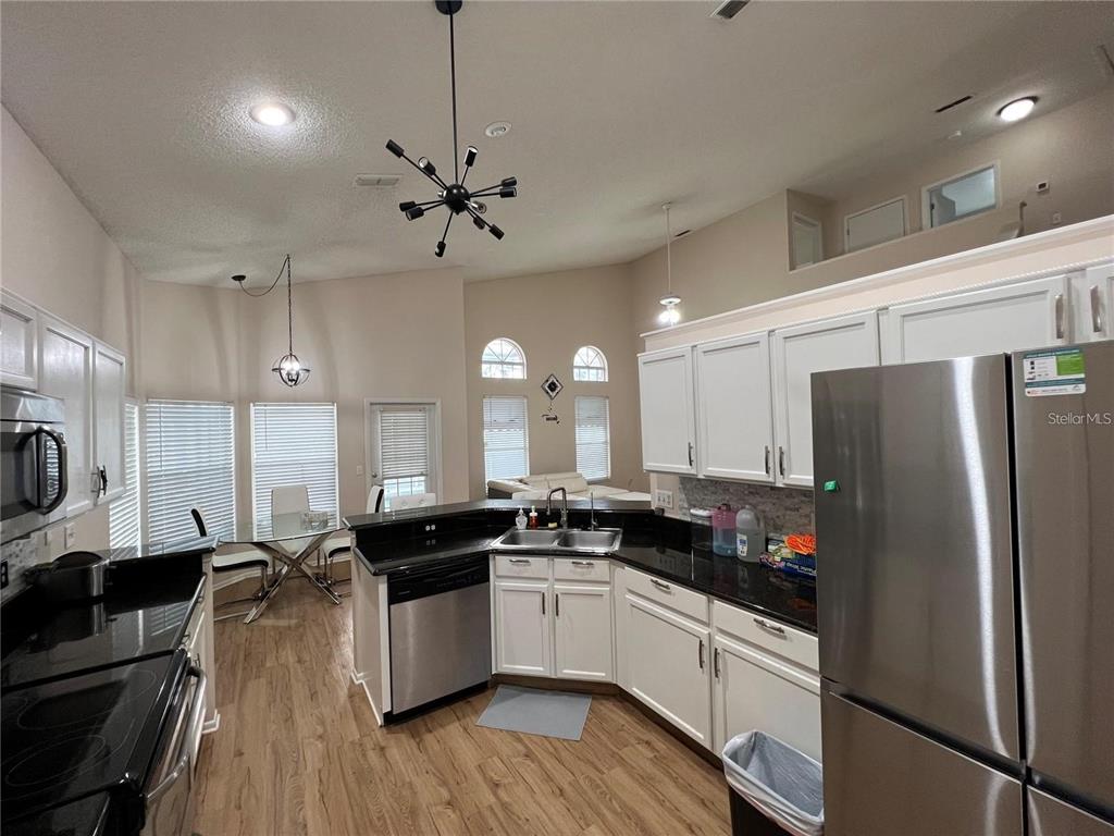 A kitchen with white cabinets, black countertops, stainless steel appliances, and an adjacent dining area — 755 RIGGS CIRCLE, DAVENPORT, FL