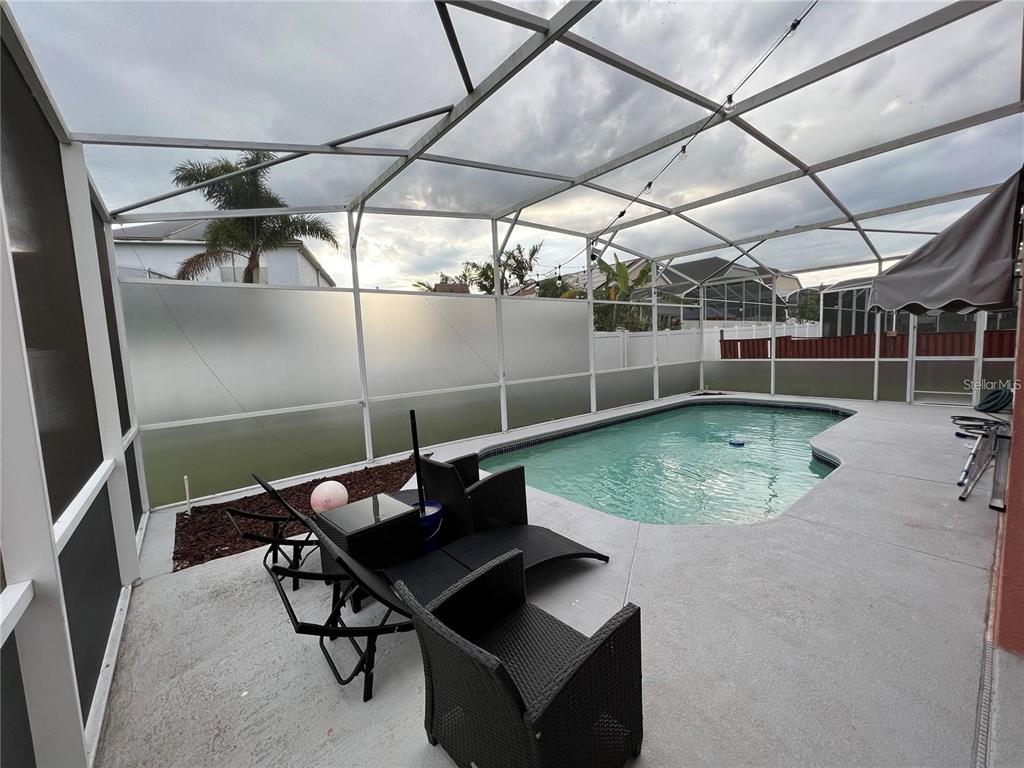 A screened-in patio features a swimming pool, outdoor furniture, and a privacy screen — 755 RIGGS CIRCLE, DAVENPORT, FL