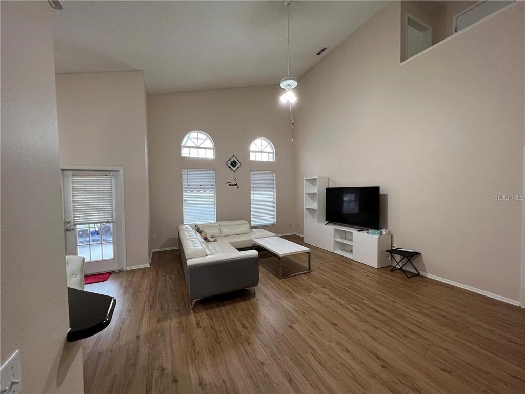 A living room features high ceilings, wood-look flooring, a white sectional sofa, and a television — 755 RIGGS CIRCLE, DAVENPORT, FL