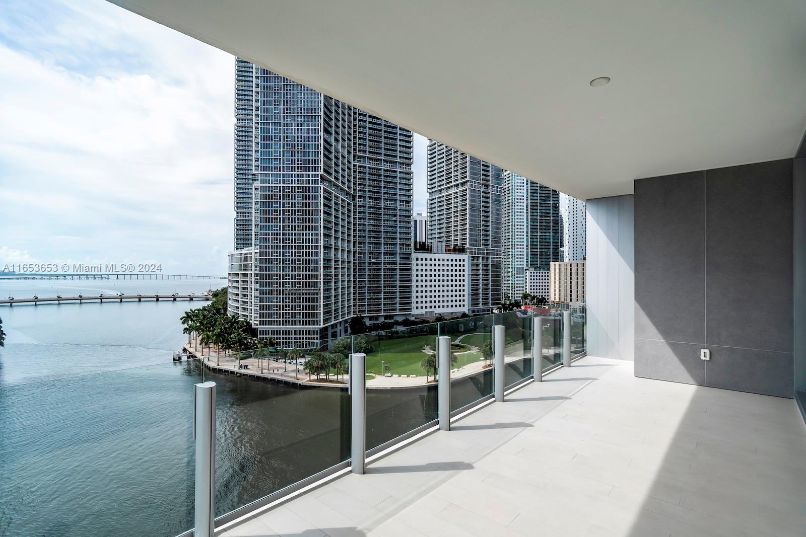 A modern balcony with a glass railing overlooks a waterfront park and city skyscrapers — 300 Biscayne Blvd Way # 902, Miami FL 33131, MIAMI, FL