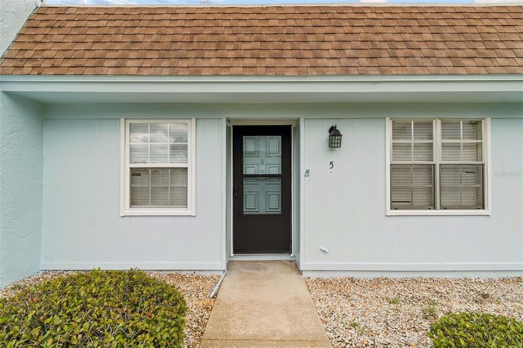 The exterior of a light blue single-story home features a brown shingled roof and walkway — 11110 CARRIAGE HILL DRIVE UNIT 5, PORT RICHEY, FL