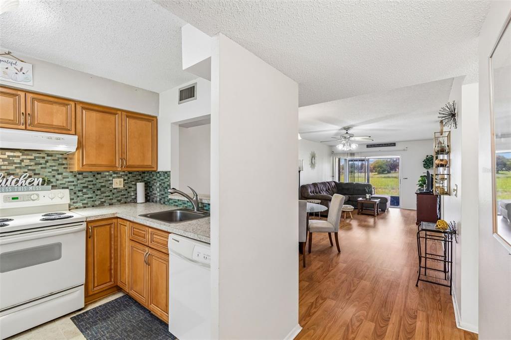 A kitchen with wood cabinets and a tiled backsplash opens into a living room area — 11110 CARRIAGE HILL DRIVE UNIT 5, PORT RICHEY, FL