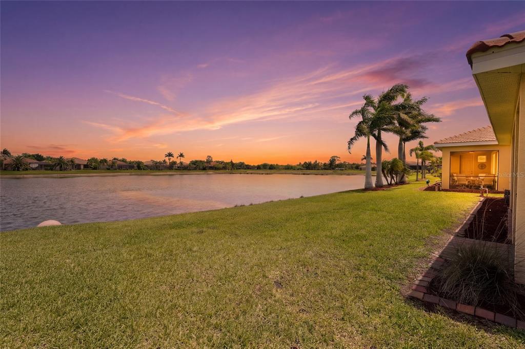A grassy backyard overlooks a lake at sunset with a covered patio and palm trees — 7360 TALON BAY DRIVE, NORTH PORT, FL