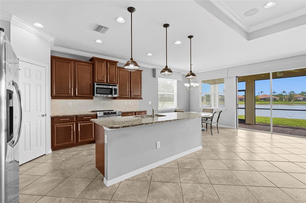 A kitchen with brown cabinets, granite countertops, an island, and a view of a lake — 7360 TALON BAY DRIVE, NORTH PORT, FL