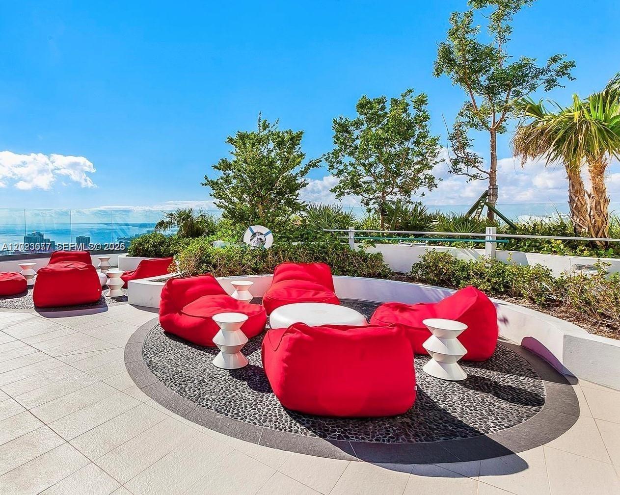 An outdoor rooftop lounge area features red beanbag chairs and white tables on a patio — 45 SW 9th St # 3501, Miami FL 33130, MIAMI, FL
