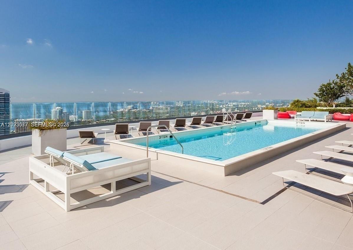 A rooftop swimming pool with lounge chairs overlooks a city skyline under a clear sky — 45 SW 9th St # 3501, Miami FL 33130, MIAMI, FL