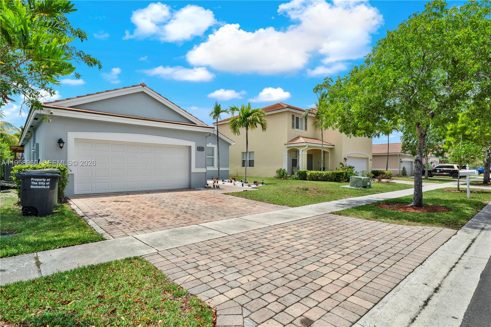 A gray single-story house with a brick driveway sits next to a yellow two-story home — 3472 NE 2nd St, Homestead FL 33033, HOMESTEAD, FL
