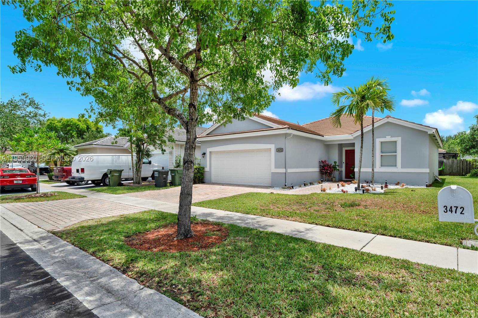 A single-story suburban house with a gray exterior, a two-car garage, and a red door — 3472 NE 2nd St, Homestead FL 33033, HOMESTEAD, FL