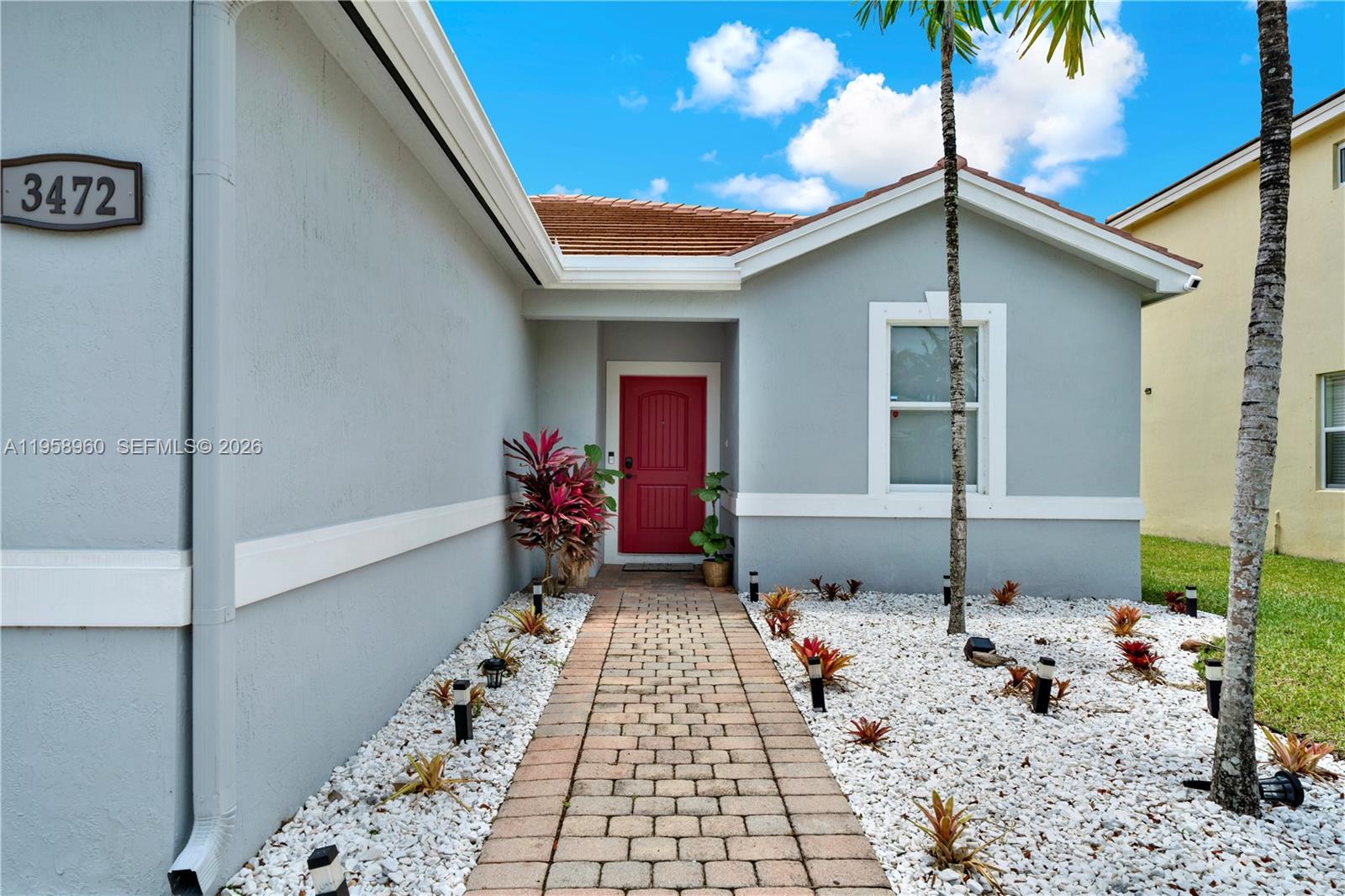 A light gray house features a red front door and a brick walkway — 3472 NE 2nd St, Homestead FL 33033, HOMESTEAD, FL