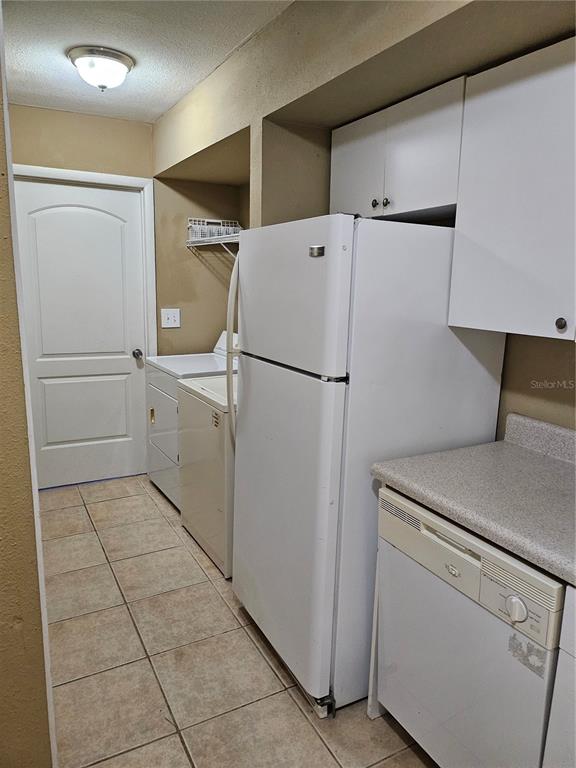 A kitchen area features a white refrigerator, dishwasher, and laundry appliances on a tiled floor — 6640 POT O GOLD LANE, ORLANDO, FL