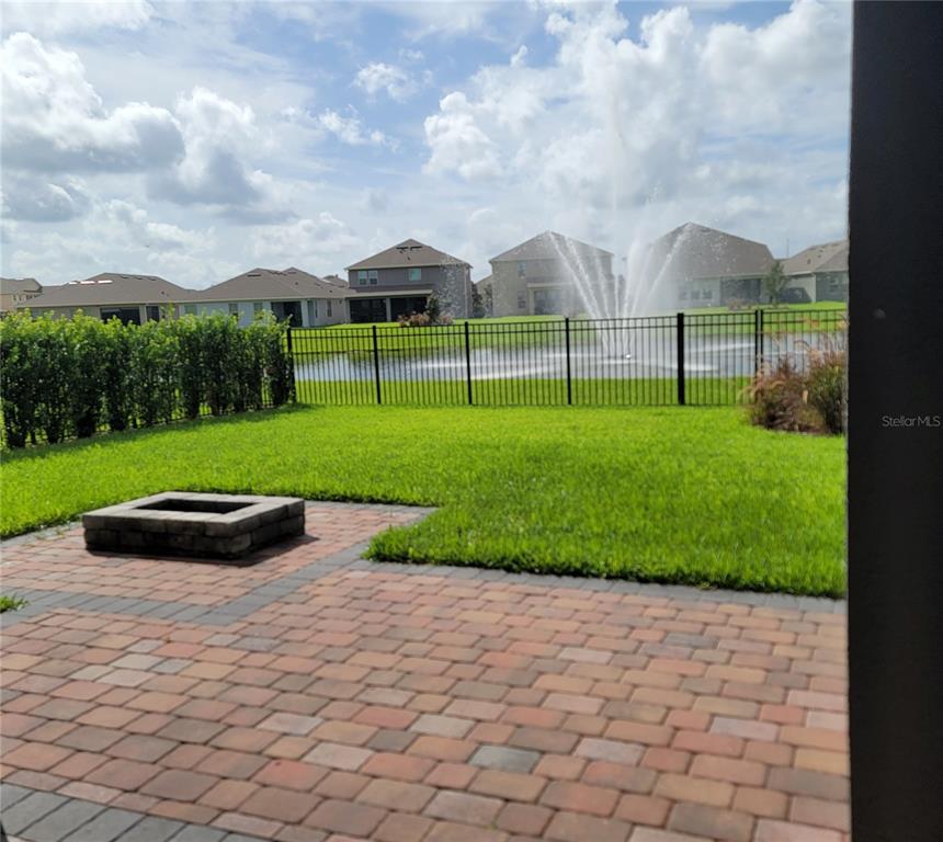 A backyard patio with a fire pit overlooks a pond with a fountain and houses — 16124 AZURE KEY STREET, WINTER GARDEN, FL