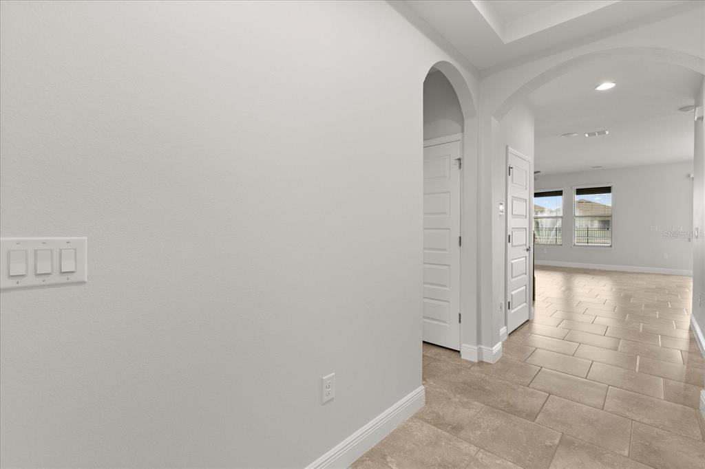 A hallway with light tile flooring leads to an open living area with arched doorways — 16124 AZURE KEY STREET, WINTER GARDEN, FL