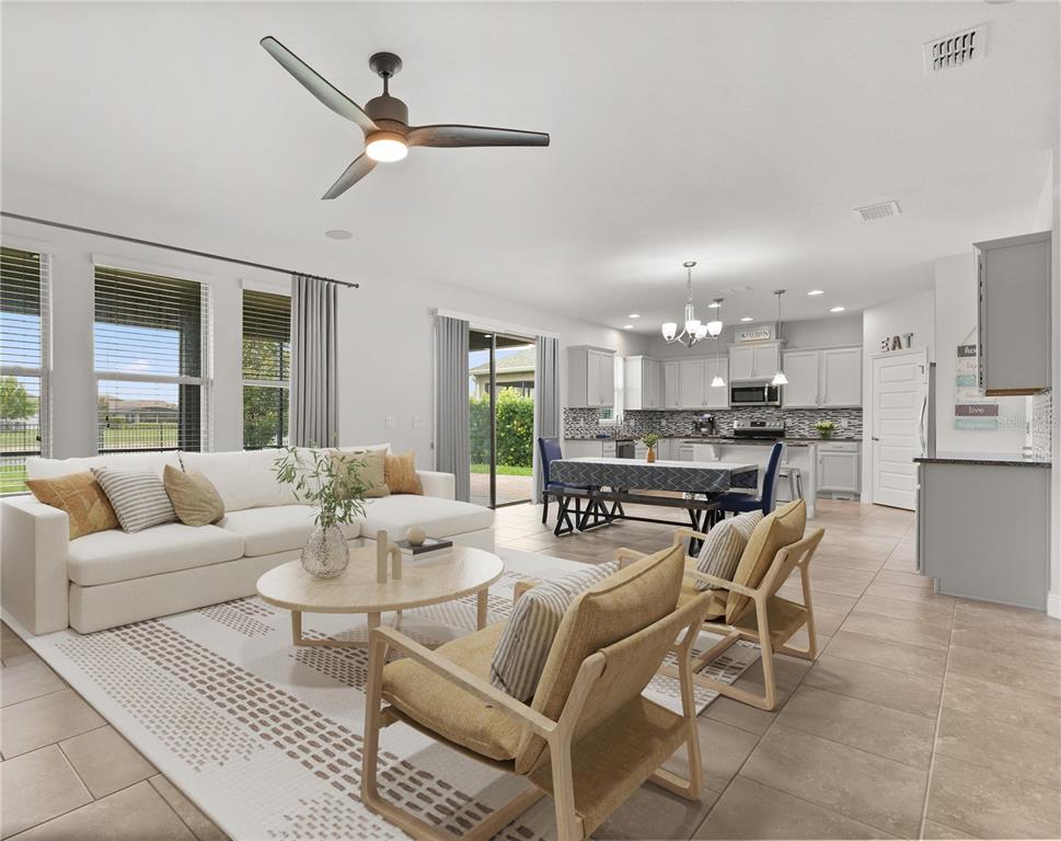 An open-concept living room and kitchen featuring tile floors, a ceiling fan, and neutral decor — 16124 AZURE KEY STREET, WINTER GARDEN, FL
