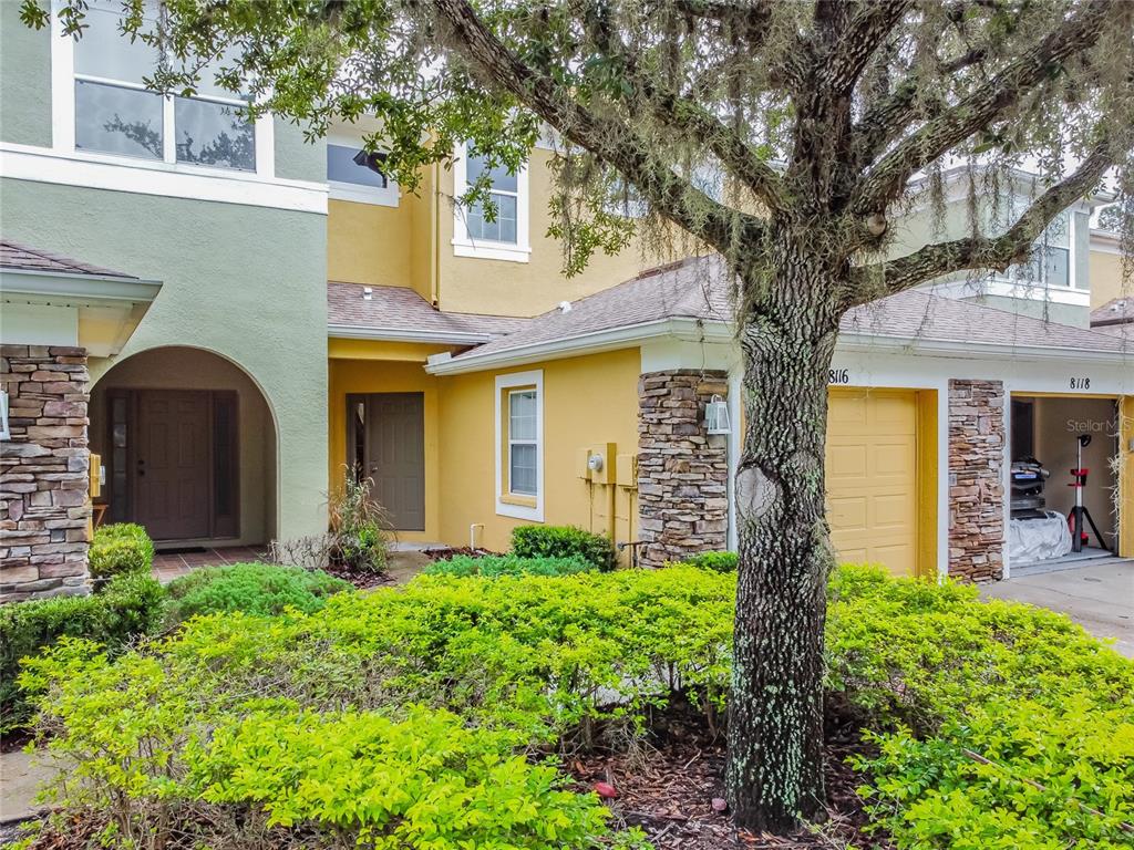 A two-story house exterior features yellow and green stucco walls, stone accents, and a garage — 8116 STONE PATH WAY, TAMPA, FL