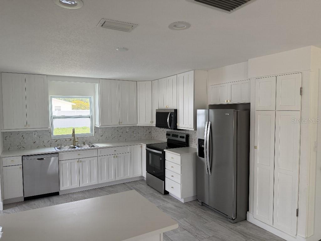 A kitchen with white cabinets, stainless steel appliances, a gray island, and light tile flooring — 632 89TH AVENUE N, ST PETERSBURG, FL