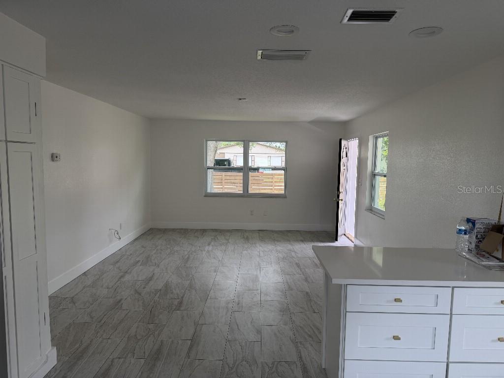 A bright living area features light-colored wood-look tile flooring, white walls, and a kitchen island — 632 89TH AVENUE N, ST PETERSBURG, FL
