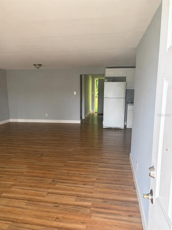 An interior view shows a living area with wood-look flooring leading to a kitchen with a refrigerator — 407 S ANDERSON STREET, BUNNELL, FL