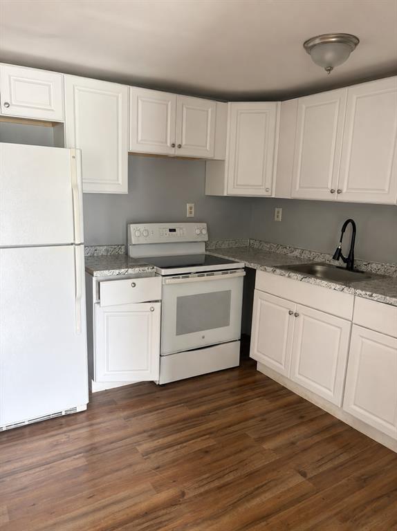 A kitchen features white cabinets, granite countertops, a white stove, a refrigerator, and wood flooring — 407 S ANDERSON STREET, BUNNELL, FL
