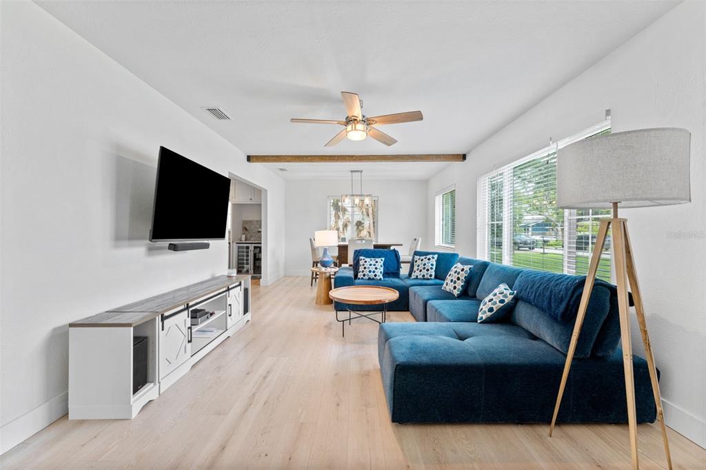A bright living room features a blue sectional sofa, wood flooring, and a wall-mounted television — 802 W CORAL STREET, TAMPA, FL