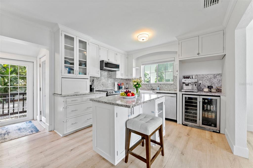 A white kitchen features a granite-topped island, light wood flooring, and a built-in wine cooler — 802 W CORAL STREET, TAMPA, FL