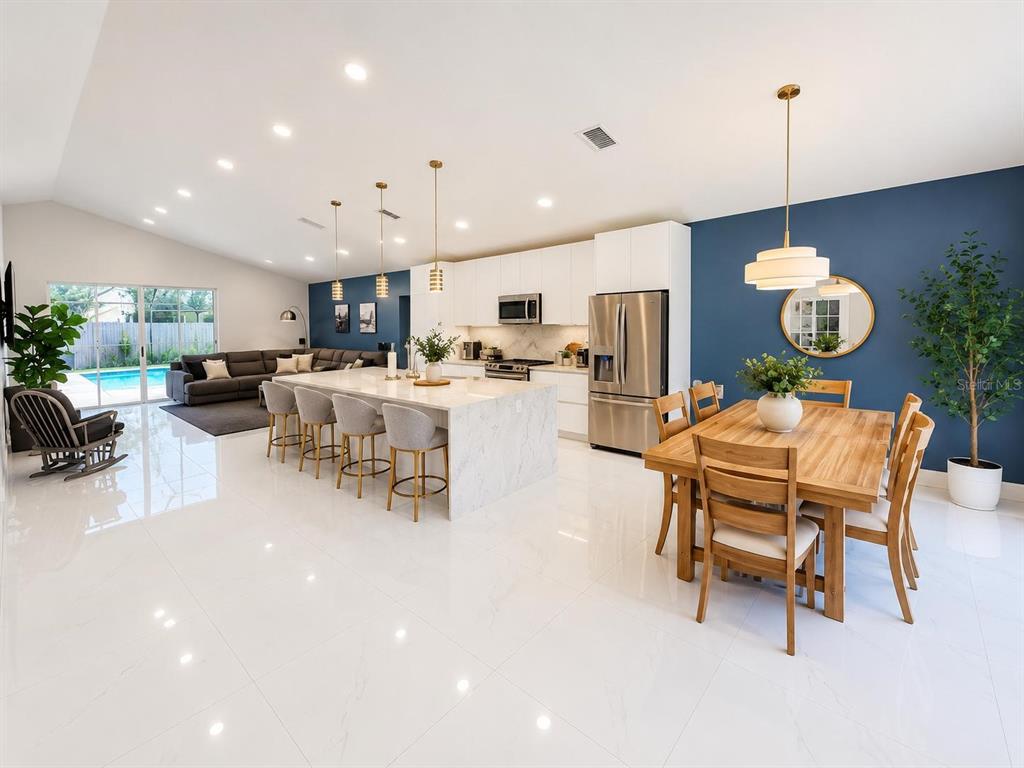 A bright open-concept kitchen and dining area features white marble floors, a large island, and blue walls — 3728 COLD CREEK DRIVE, VALRICO, FL
