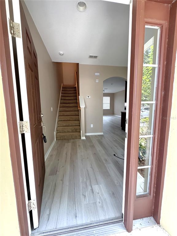 An entryway features light wood-look flooring, a carpeted staircase, and a view into the home — 12937 EMERSONDALE AVENUE, WINDERMERE, FL