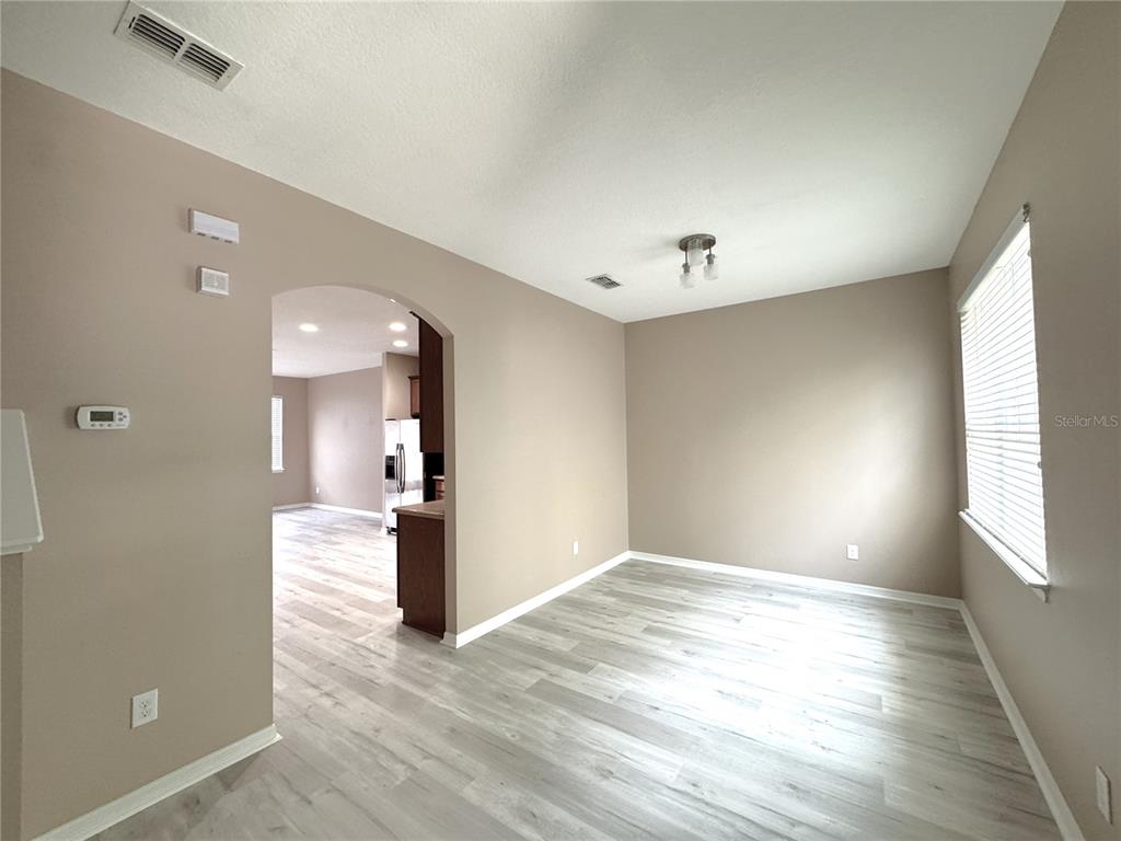 An empty room with light-colored wood-look flooring and an arched doorway leading to a kitchen — 12937 EMERSONDALE AVENUE, WINDERMERE, FL