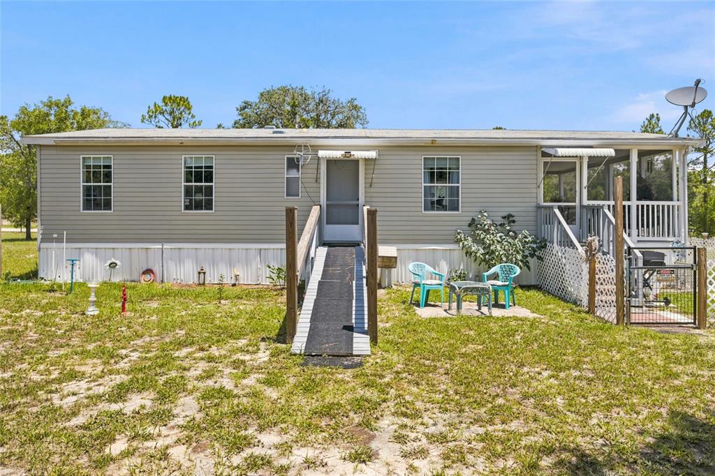 A single-story manufactured home with light siding, a wheelchair ramp, and a screened-in porch — 13330 SE 21ST PLACE, MORRISTON, FL