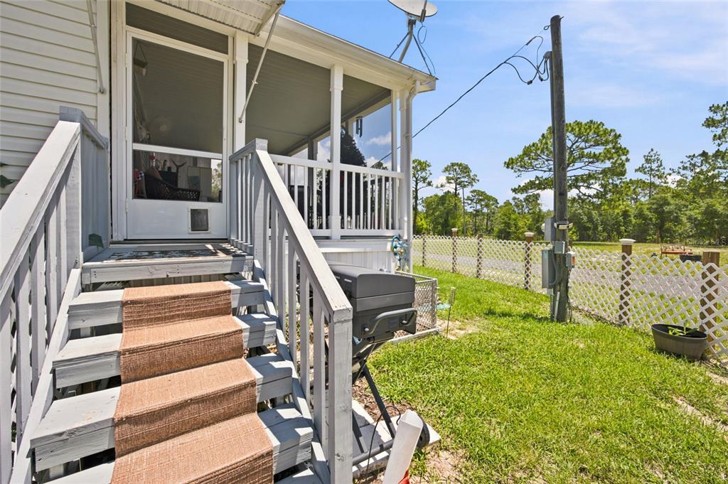 A wooden staircase with a brown runner leads to a screened porch with a grill — 13330 SE 21ST PLACE, MORRISTON, FL