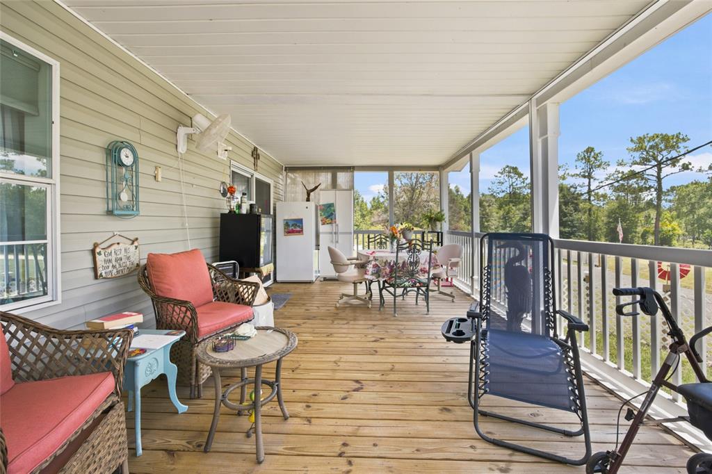 A spacious covered wooden deck features outdoor seating, a dining table, and a white refrigerator — 13330 SE 21ST PLACE, MORRISTON, FL