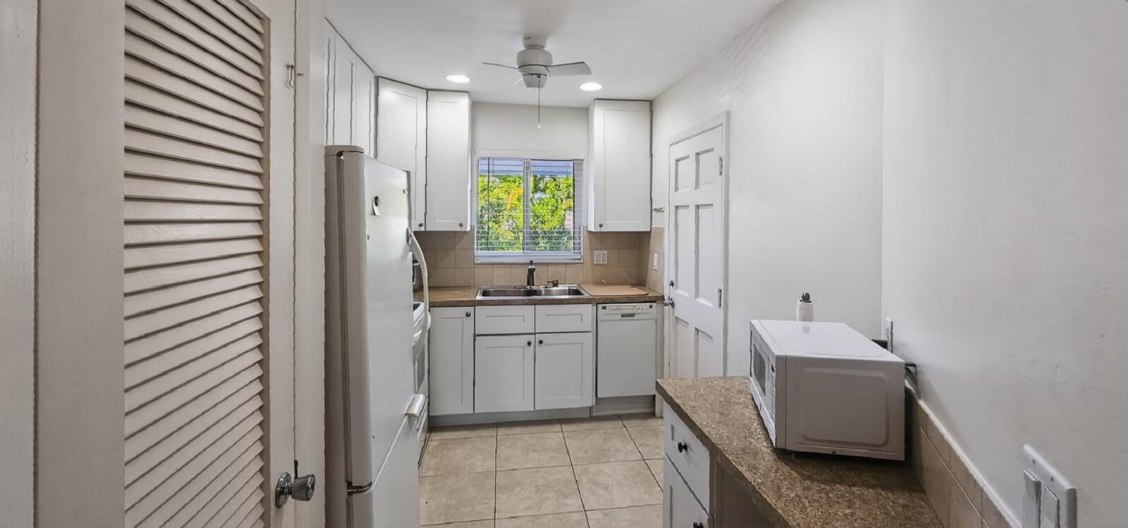 A galley-style kitchen features white cabinets, a window above the sink, and tile flooring — 8 Garden Street # 206r, Tequesta FL 33469, TEQUESTA, FL