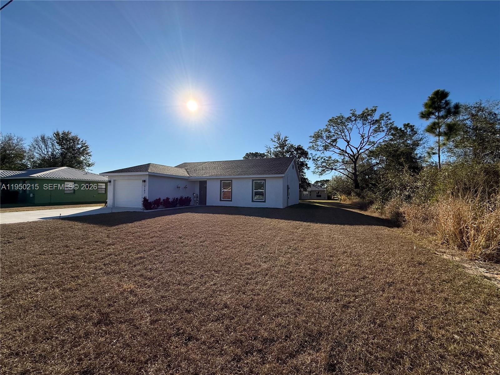 A single-story white house with a garage sits on a large, dry grassy lot — 4103 Loretto Ave, Sebring FL 33872, SEBRING, FL
