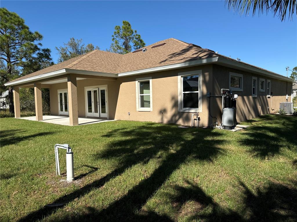 The exterior of a tan stucco house features a covered patio and a well pump — 1409 MARJORIE LANE, NORTH PORT, FL