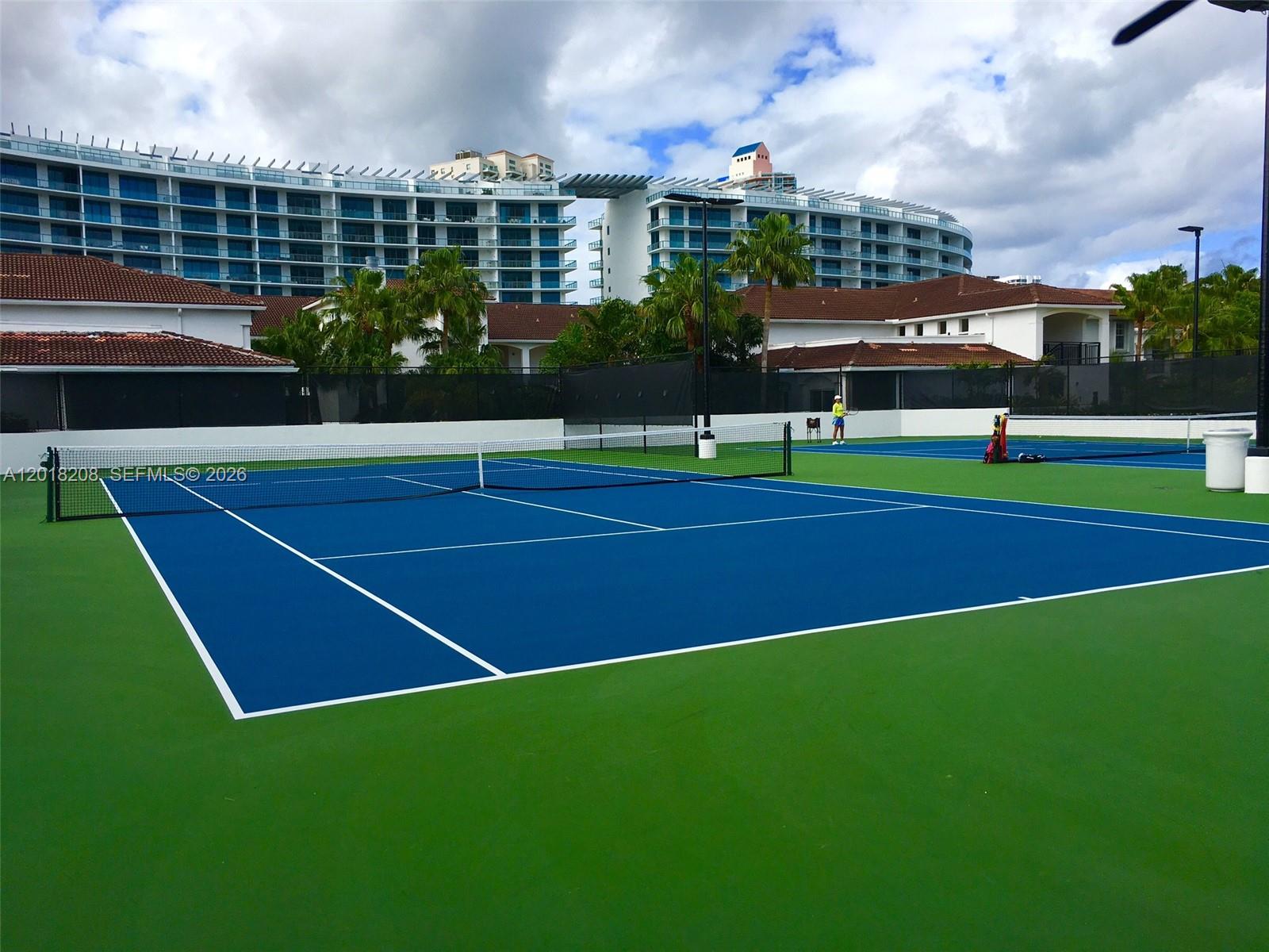 A blue and green tennis court sits in front of a large residential building — AVENTURA, FL