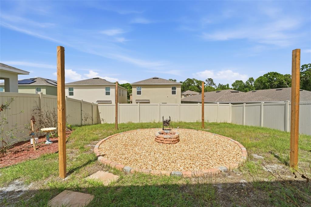 A backyard features a circular gravel fire pit area surrounded by four tall wooden posts — 1356 BERRY LANE, DAVENPORT, FL