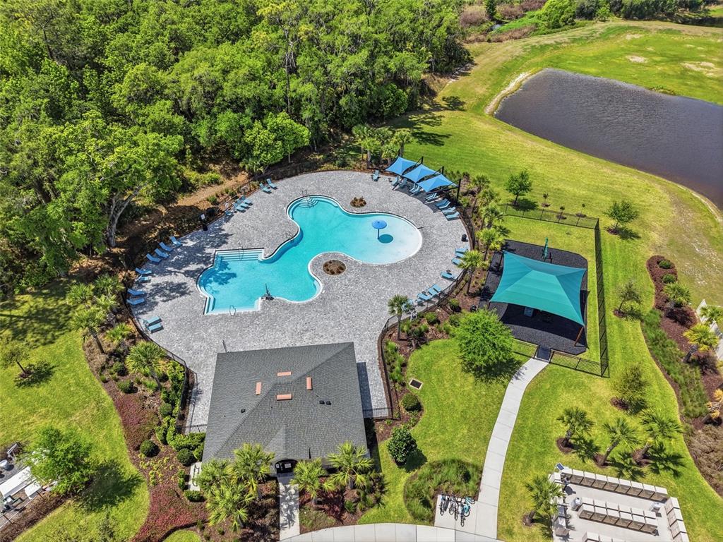 An aerial view shows a swimming pool with a clubhouse, playground, and pond nearby — 1356 BERRY LANE, DAVENPORT, FL