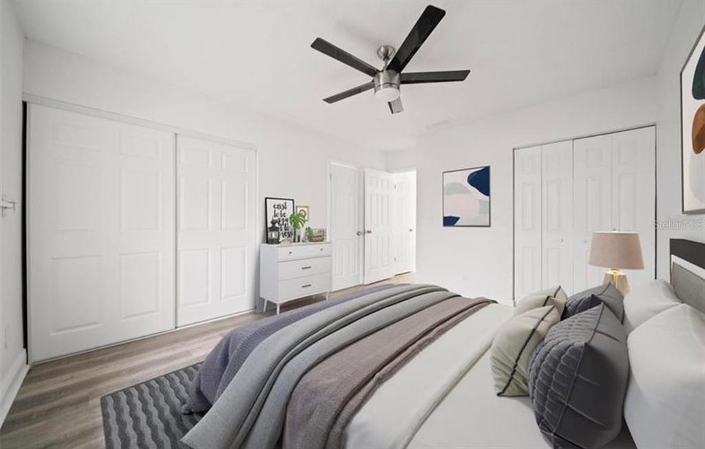 A bedroom features white walls, a ceiling fan, light wood flooring, and two white closets — 7013 SALINAS COURT, TAMPA, FL