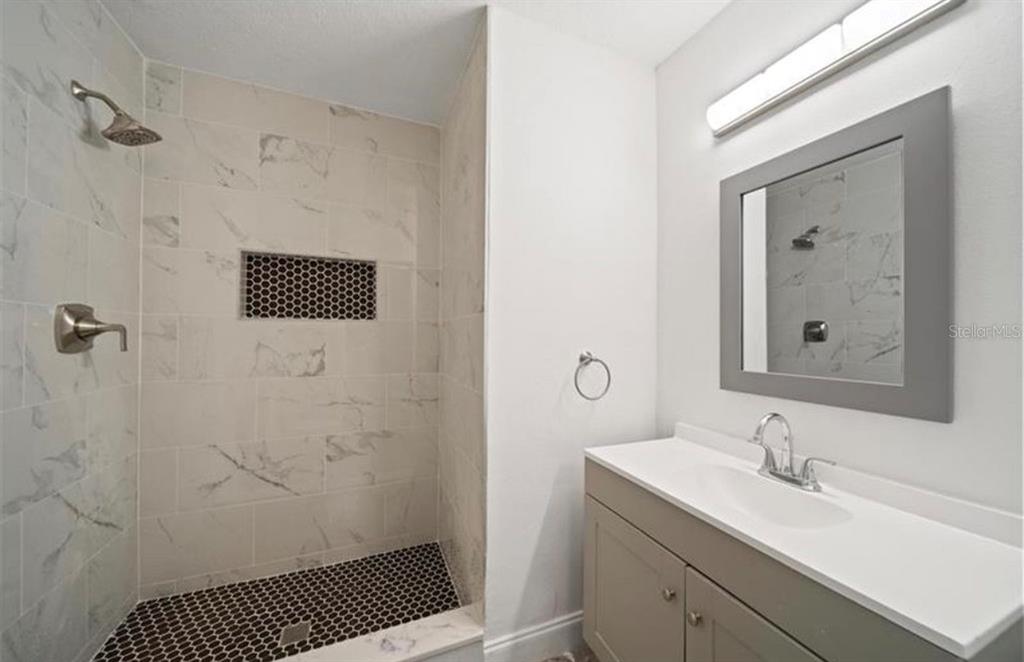 A bathroom features a walk-in shower with marble-look tile, a vanity, and a gray-framed mirror — 7013 SALINAS COURT, TAMPA, FL