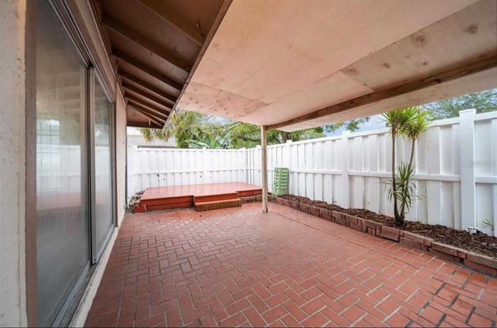A covered brick patio features a small wooden deck and a white privacy fence — 7013 SALINAS COURT, TAMPA, FL