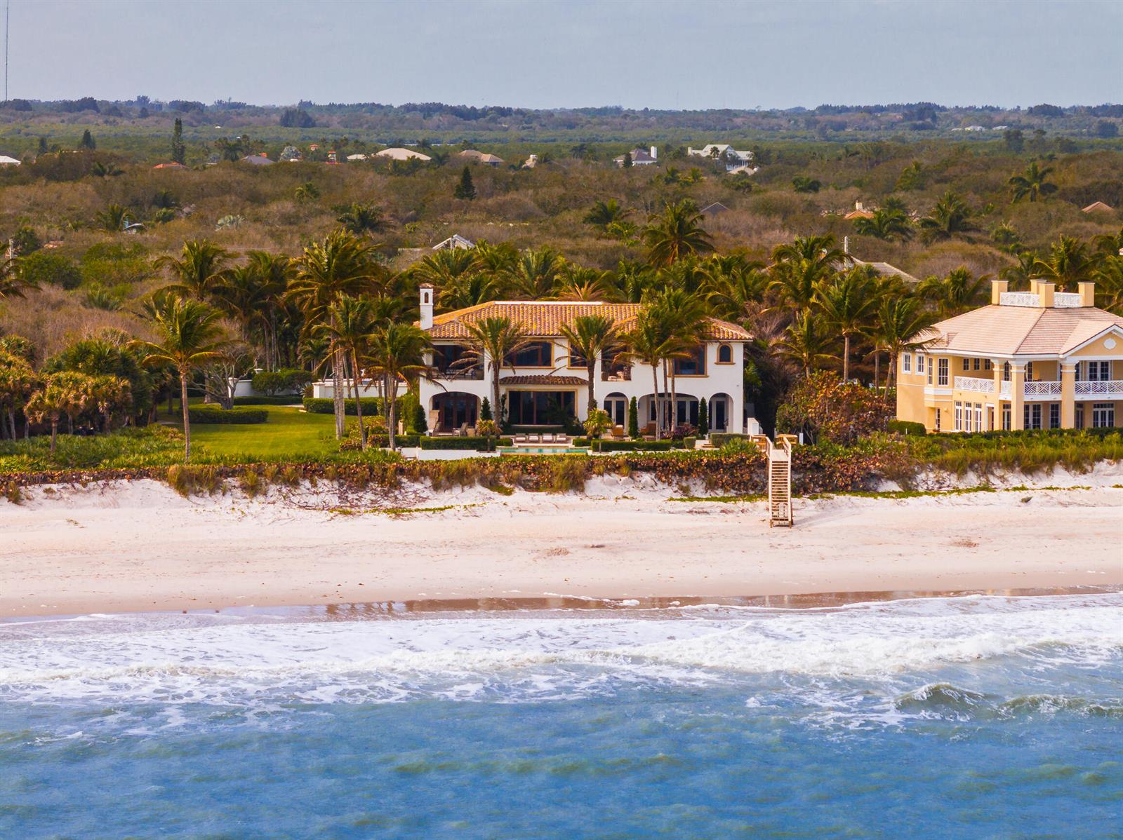 An aerial view of a beachfront Mediterranean-style house with palm trees and a sandy shore — 10 Ocean Lane, Vero Beach FL 32963, VERO BEACH, FL