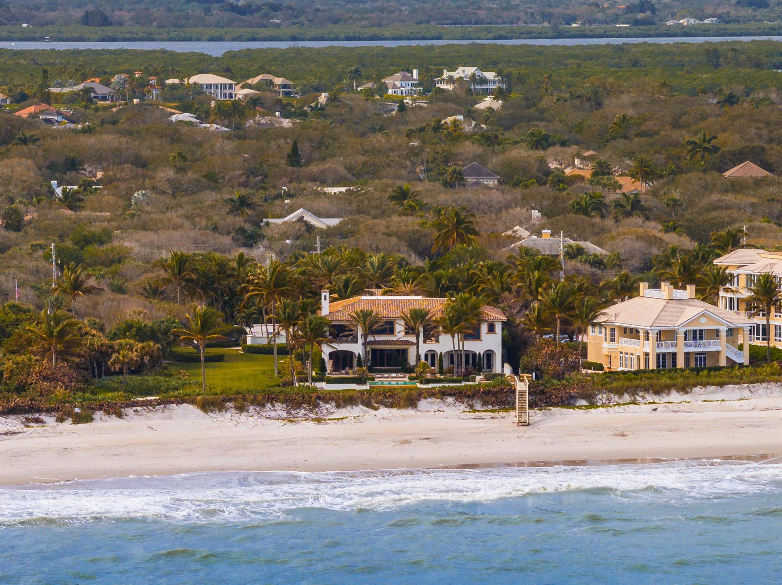 An aerial view of beachfront houses surrounded by lush tropical vegetation along a sandy shore — 10 Ocean Lane, Vero Beach FL 32963, VERO BEACH, FL