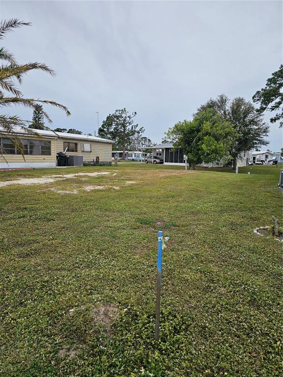 A vacant grassy lot sits between two mobile homes under a cloudy sky — 6811 HOLO COURT, NORTH PORT, FL