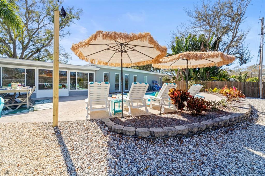 A backyard patio features a pool, lounge chairs under straw umbrellas, and a gravel area — 13347 88TH PLACE, SEMINOLE, FL